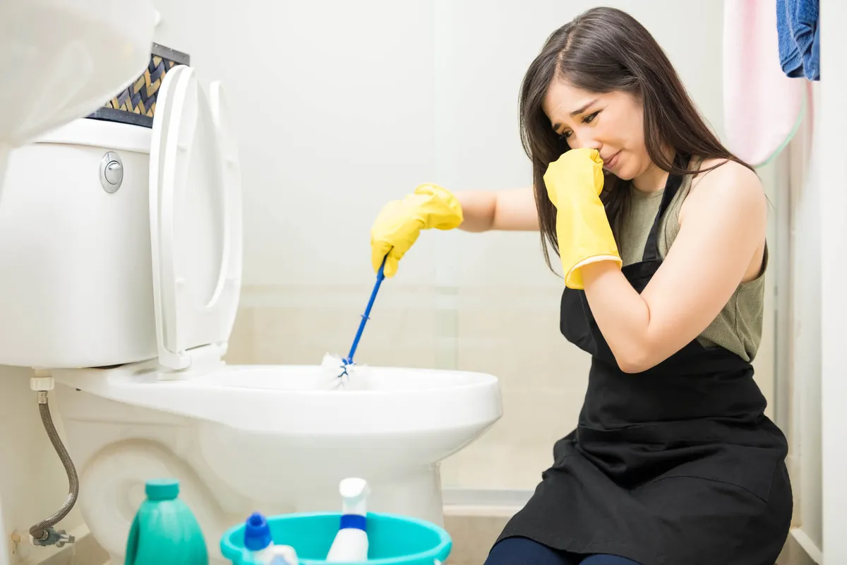 Mulher de luvas limpando o vaso sanitário do banheiro